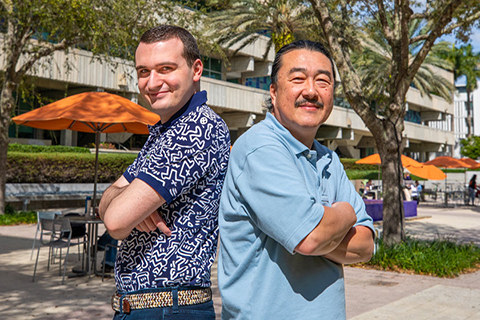 This photo was taken at the University of Miami Coral Gables campus. Dr. Mitsunori Ogihara is standing back-to-back with a Ph.D candidate. They are standing in the courtyard of the Cox Science Center. 